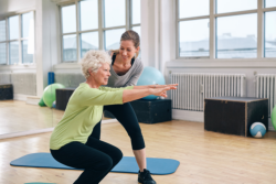 staff with old woman having hip exercise session